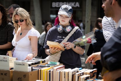 Una joven con una rosa revisa la portada de un libro en uno de los puestos de la feria de Sant Jordi, en Barcelona.