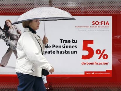 Una mujer camina frente a una sucursal bancaria en la que se anuncian planes de pensiones.