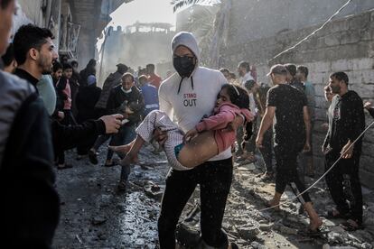 Un hombre transporta a una niña, mientras la gente busca más víctimas entre los escombros de un edificio destruido, a causa de un bombardeo israelí, este viernes en Jan Yunis.  
