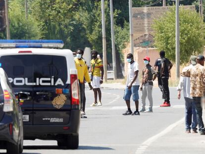 Varios residentes en el asentamiento de la carretera de Peñas, ante vehículos de Policía Nacional.