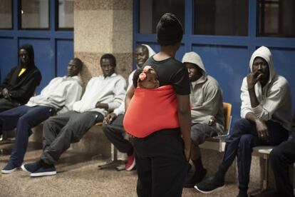 Una mujer pasea con su bebé a la espalda frente a un grupo de migrantes sentados en la sala de espera de la Estación Marítima de Algeciras.