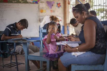 Una niña desayuna en clase mientras su madre le ayuda a hacer los deberes.