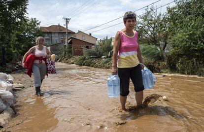 Dos mujeres sostienen agua embotellada y pan mientras caminan por una calle inundada en el pueblo.