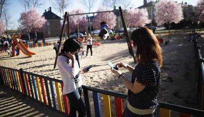 Dues dones fan servir el mòbil al costat d'un parc infantil.