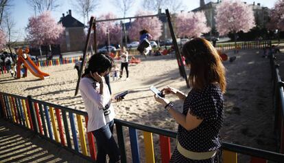 Dos mujeres usan su tel&eacute;fono m&oacute;vil al lado de un parque infantil