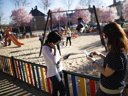 Dues dones fan servir el mòbil al costat d'un parc infantil.