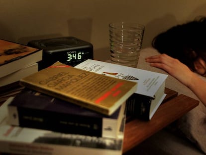 Una mujer durmiendo, con varios libros en la mesilla, junto al reloj despertador. 