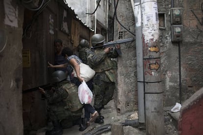 Mulher desliza entre soldados para ultrapassar uma barreira armada em um beco da Rocinha.