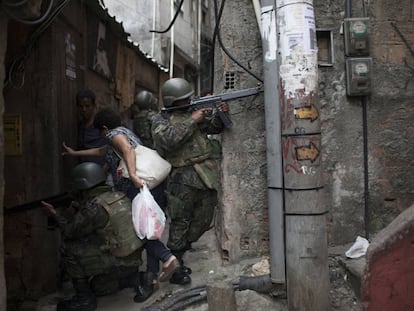 Mulher desliza entre soldados para ultrapassar uma barreira armada em um beco da Rocinha.