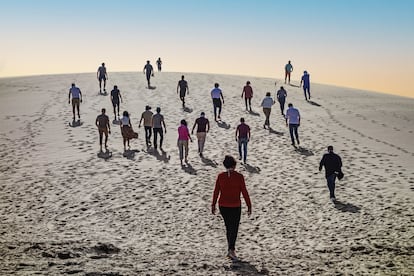 Varios turistas subiendo a lo alto de la Duna Blanca, una montaña de arena blanca donde el Sáhara y el Atlántico se funden.