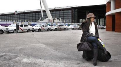 Una pasajera espera sentada sobre su maleta en la estación de Atocha, con una fila de taxis parados al fondo.