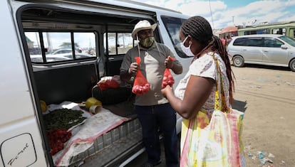 El guía turístico y ahora frutero Anthony Mwai, de 40 años, vende unas mallas de cebollas a una clienta en Nairobi en su frutería ambulante.