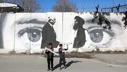 Dos niños afganos juegan frente a un mural con las imágenes de Zalmay Khalilzad (a la derecha), enviado especial de EE UU en Afganistán, y Mullah Abdul Ghani Baradar, líder de la delegación talibán, en el primer aniversario del acuerdo entre los Estados Unidos y los talibanes, en Kabul (Afganistán), este sábado.