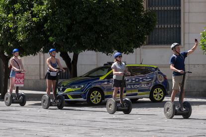 Un grupo de turistas, junto a coche de la Policía Local de Sevilla. 