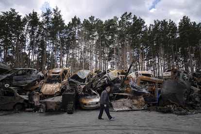Un hombre pasa frente a un lugar de almacenamiento de vehículos y automóviles armados quemados, en las afueras de Kiev.