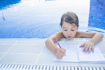 Una niña haciendo deberes en la piscina.