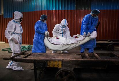 Varios sanitarios trasladan el cuerpo de un fallecido por coronavirus para su incineración, en el crematorio Nigambodh, en Nueva Delhi (India).
