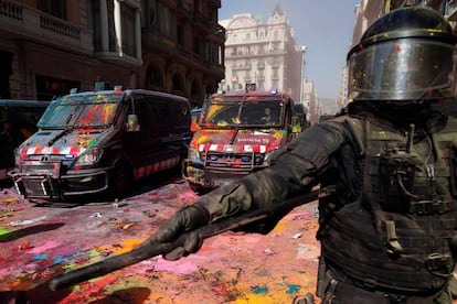 Un 'mosso', este sábado en Barcelona. Al fondo, dos furgonetas cubiertas de pintura lanzada por los manifestantes.