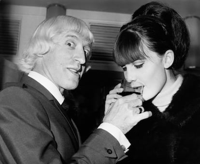 English singer Sandie Shaw accepts a drink from disc jockey Jimmy Savile (1926 - 2011) at a Variety Club of Great Britain luncheon  at the Savoy Hotel in London, 14th September 1965. They were voted Best Female Singer and Best Disc Jockey respectively, by readers of music journal 'Melody Maker'. (Photo by J. Wilds/Keystone/Hulton Archive/Getty Images)