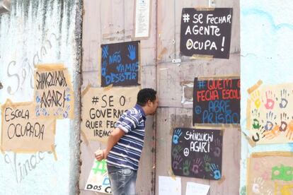 Homem olha pelo port&atilde;o de uma escola ocupada.