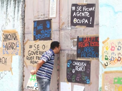 Homem olha pelo port&atilde;o de uma escola ocupada.