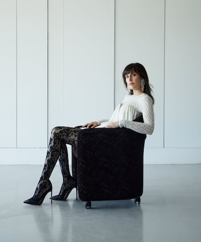 Minivestido blanco, jersey de encaje de manga larga a tono con el vestido, medias de encaje negras y maxipendientes decuentas en cascada, todo de ISABEL MARANT, y zapatos de tacón de AQUAZZURA.