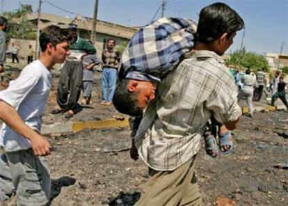 Un muchacho iraquí, que carga al hombro a un niño herido, se aleja del lugar en que explotó uno de los coches bomba que ayer sacudieron Bagdad.