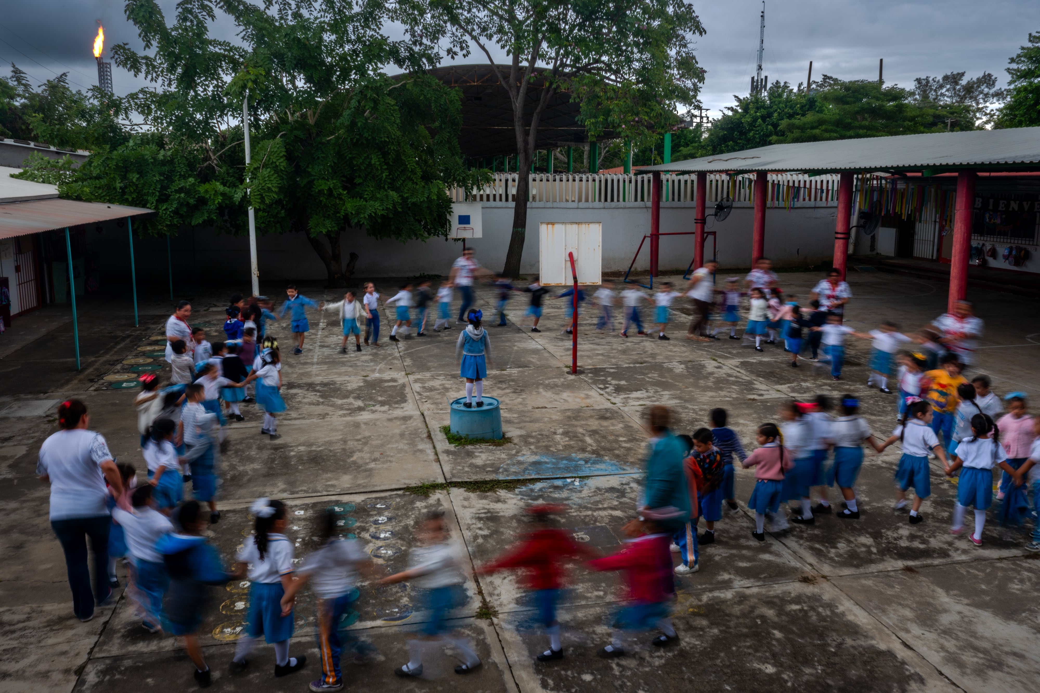 Niños juegan en el preescolar Agustín Melgar, con el mechón de la refinería Olmeca de fondo, en enero de 2026.