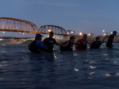 Migrantes se enlazan de brazos mientras vadean el Río Grande con intenciones de cruzar a Eagle Pass (Texas).