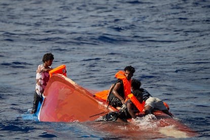 Varios migrantes se ayudan entre sí para subir a la patera volcada y permanecer a salvo.