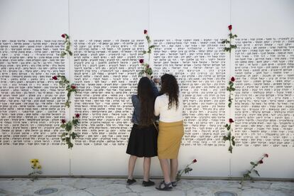 Dos chicas cuelgan rosas en una pared con los nombres de los soldados caídos, antes de la ceremonia para conmemorar a los soldados y civiles muertos en más de un siglo de conflicto entre judíos y árabes, en Latrun cerca de Jerusalén, Israel.