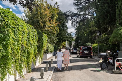 Una señora pasea de la mano de su cuidadora en una colonia de viviendas en Madrid.