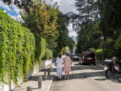 Una señora pasea de la mano de su cuidadora en una colonia de viviendas en Madrid.