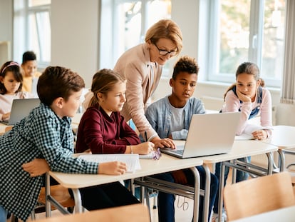 Una profesora de primaria y sus alumnos utilizan un ordenador portátil en clase.