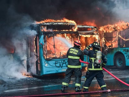 Bombeiros combatem incêndio em ônibus que foram atacados durante os protestos em Santiago.