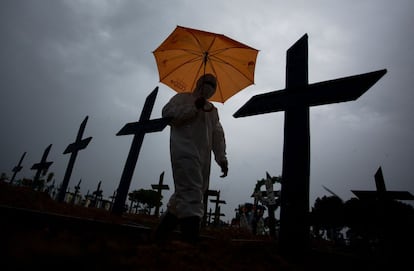 Un trabajador con traje de protección y paraguas pasa por delante de las tumbas de las víctimas por el COVID-19 en el cementerio de Nossa Senhora Aparecida, en Manaos, Brasil, el 25 de febrero de 2021. - Brasil superó las 250.000 muertes por efectos del coronavirus.