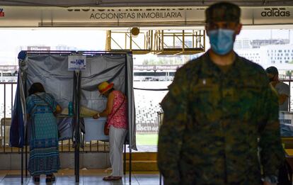 Dos mujeres votan en un colegio electoral en Santiago mientras un militar resguarda la zona.