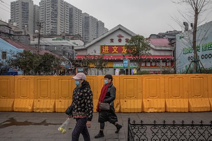 Unas mujeres con mascarilla pasan por delante de un área vallada en Wuhan.