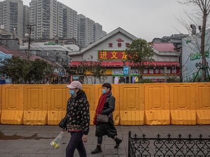 Unas mujeres con mascarilla pasan por delante de un área vallada en Wuhan.