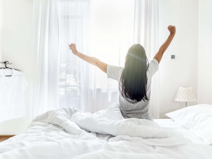 Una joven se levanta y despierta de la cama con los primeros rayos de sol.