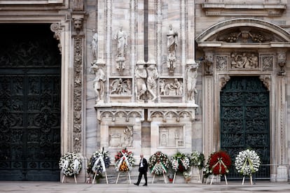 Una persona camina entre varias coronas de flores en el exterior de la catedral de Milán.
