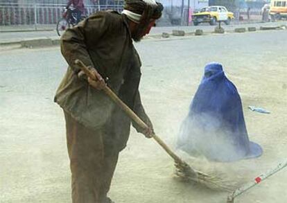 Un hombre barre el polvo de la calle hacia una mujer que pide limosna ayer en Kabul.