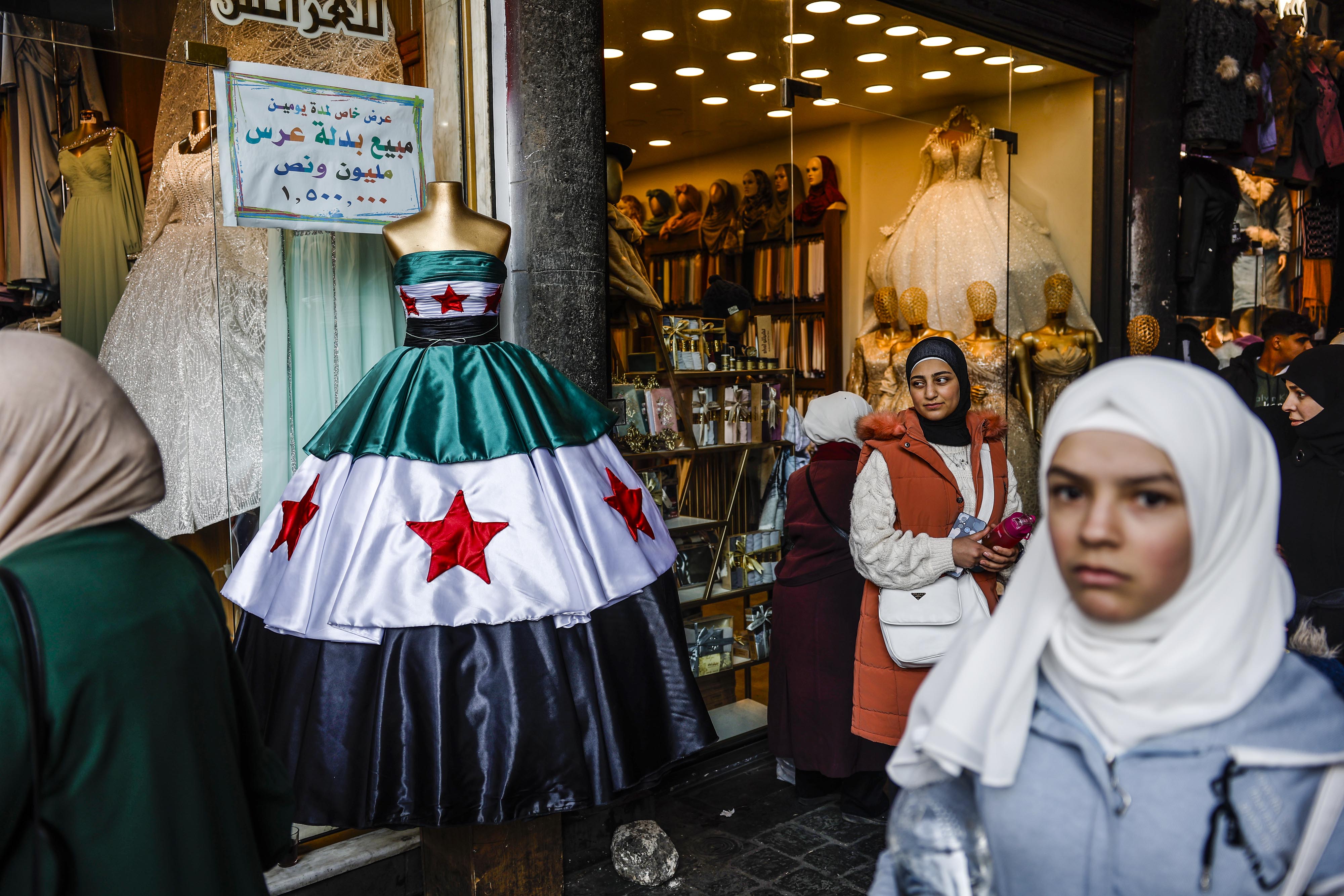 Varias personas pasan delante de un vestido con la bandera de la nueva siria en Damasco.