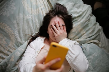 Una mujer en la cama observa su teléfono.