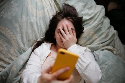 A woman in bed looks at her phone.