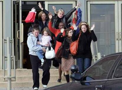 Varias mujeres salen con los brazos en alto de una de las tiendas del centro comercial.