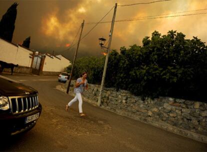 Una mujer corre por las calles de la localidad de Mombeltrán, en Ávila, mientras las llamas de acercan