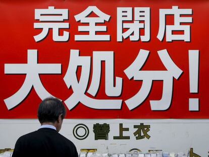 Un hombre observa el escaparate de una tienda con un cartel que anuncia grandes descuentos por cierre de negocio, en Tokio