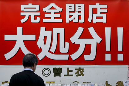 Un hombre observa el escaparate de una tienda con un cartel que anuncia grandes descuentos por cierre de negocio, en Tokio