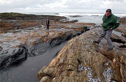 Dos hombres pasean sobre las rocas cubiertas de fuel en Porto do Son.